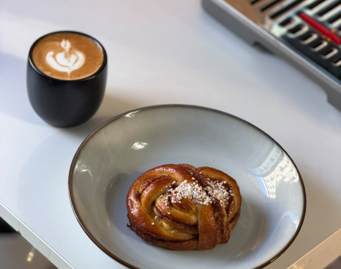 Svensk kanelbulle med pärlsocker i en skål bredvid en kaffekopp med lattekonst